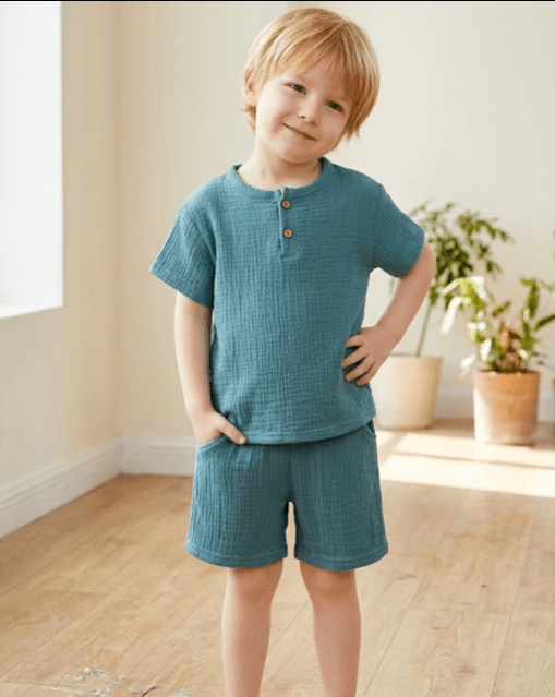 Child wearing a teal outfit standing in a room with wooden floor and plants.