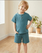 Child wearing a teal outfit standing in a room with wooden floor and plants.