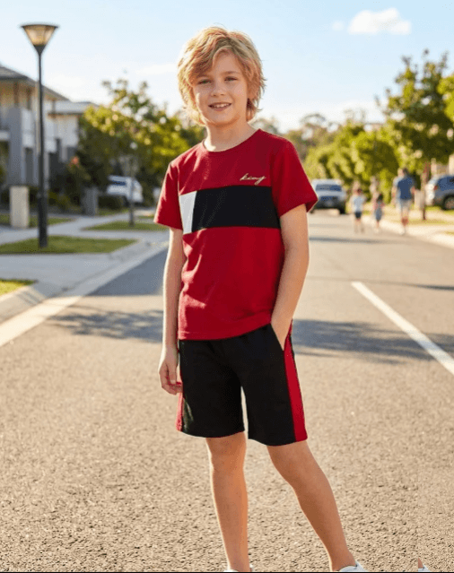 Young boy in a red and black sports outfit standing on a street.
