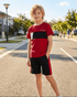 Young boy in a red and black sports outfit standing on a street.