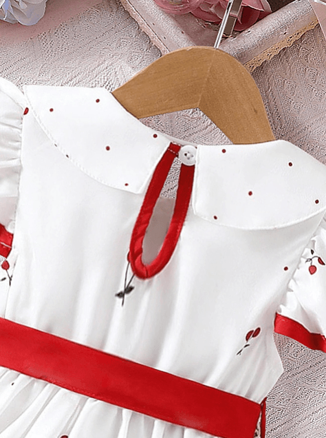 White dress with red accents on a hanger against a neutral background