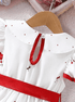 White dress with red accents on a hanger against a neutral background