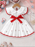 White dress with red trim and bow on a hanger, surrounded by decorative items.
