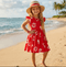 Young girl in a red dress with white floral patterns and a straw hat standing on a beach.