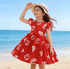 Young girl in a red dress with white floral patterns on a beach.