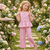 Young girl in a pink outfit holding flowers in a garden setting
