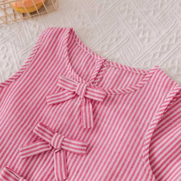Pink and white striped shirt with bow details on a textured surface