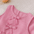 Pink and white striped shirt with bow details on a textured surface