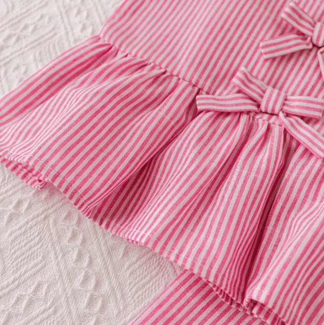 Close-up of a pink and white striped dress with a bow on a textured white background