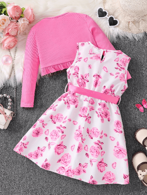 Pink sweater and floral dress on a textured surface with decorative elements.