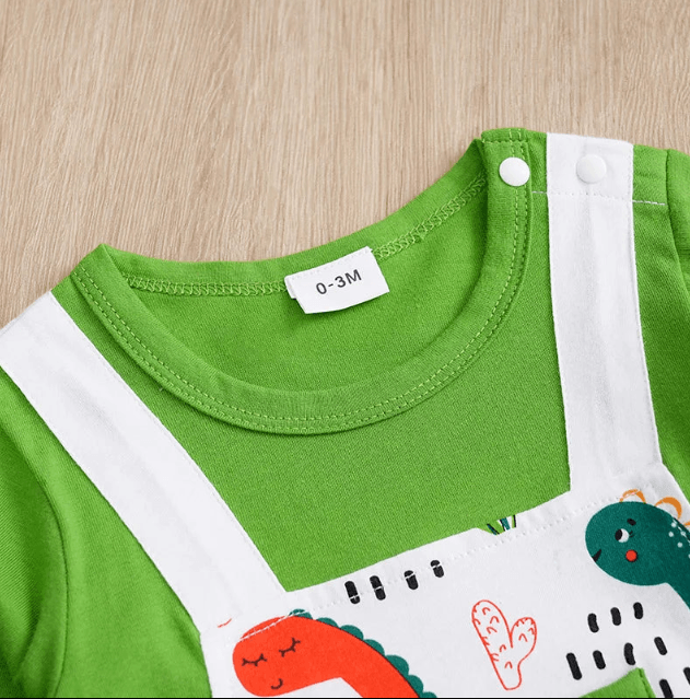 Close-up of a green and white baby outfit with dinosaur illustrations on a wooden surface.