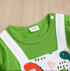 Close-up of a green and white baby outfit with dinosaur illustrations on a wooden surface.