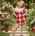 Young girl in a red and white checkered dress standing in a garden with flowers and plants.