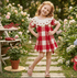 Young girl in a red and white checkered dress standing in a garden with flowers and plants.