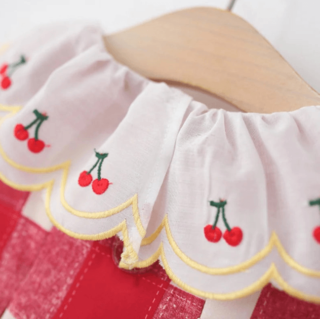 White fabric with red cherries and yellow scalloped edges on a white background