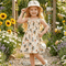 Young girl in a garden wearing a dress with bee pattern and a matching hat.