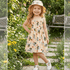 Young girl in a floral dress and sun hat standing in a garden.
