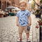 Child wearing a blue shirt with feather pattern and beige shorts on a cobblestone street.