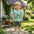 Child wearing a green t-shirt with a cartoon alligator design in a garden setting.