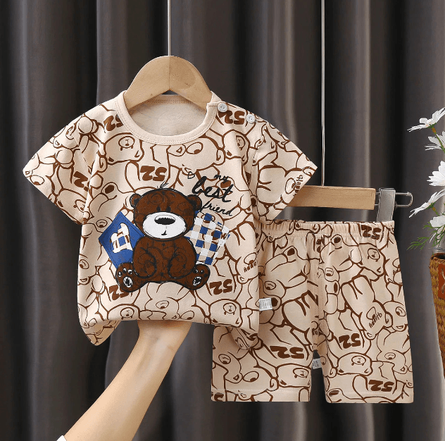 Children's clothing set with teddy bear design on a hanger against a dark curtain background.
