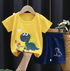 Yellow t-shirt with dinosaur design and blue shorts on a hanger against a dark background.