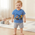 Child wearing a blue and white striped shirt with a truck design, standing on a wooden floor.