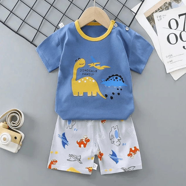 Children's blue t-shirt with dinosaur design and white shorts on a gray surface.