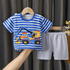 Children's blue and white striped shirt with a construction vehicle design and white shorts on a hanger against a dark curtain background.