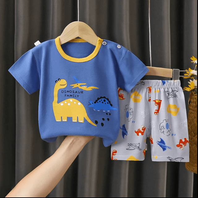 Children's blue t-shirt with dinosaur design and gray shorts with animal prints on a hanger against a dark curtain background.