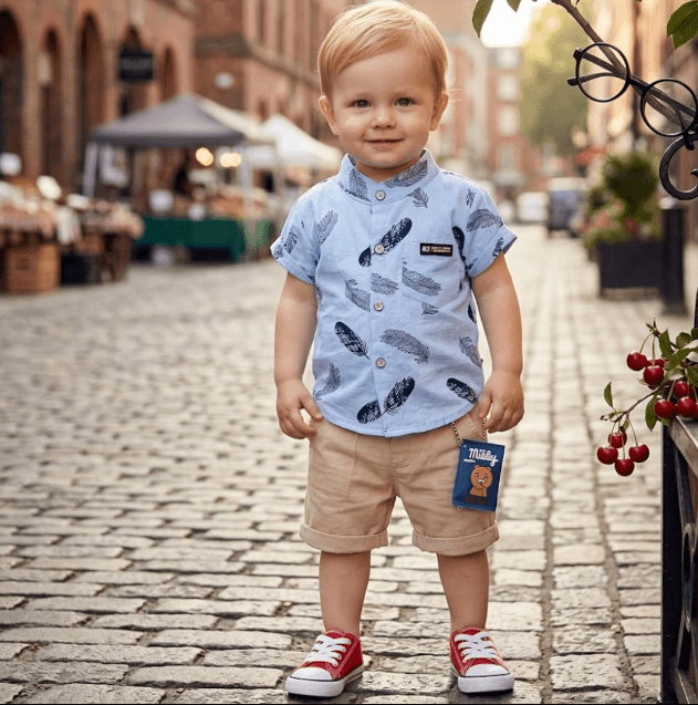 Child wearing a blue shirt with feather pattern and beige shorts on a cobblestone street.