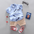 Children's outfit with blue shirt, beige shorts, red sneakers, and glasses on a gray background.