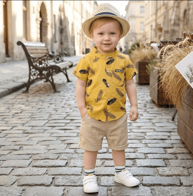 Child in a yellow shirt and shorts standing on a cobblestone street.