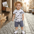 Child wearing a white shirt with feather pattern and blue shorts on a cobblestone street.