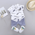 Baby outfit with white shirt and shorts, socks, and hat on a gray background