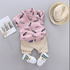 Children's pink shirt with feather pattern, beige shorts, white shoes, and a straw hat on a gray background.