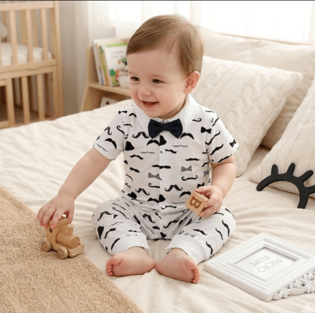 Baby in a white outfit with black patterns sitting on a bed.