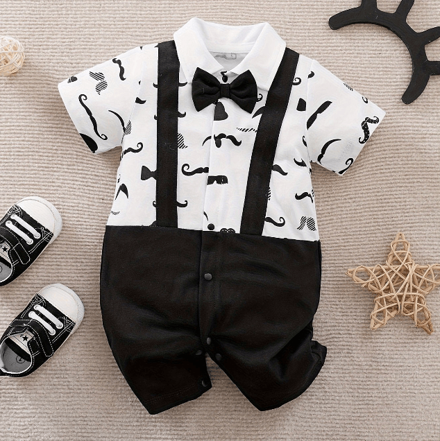 Baby outfit with white shirt, black suspenders, and bow tie on a beige surface.