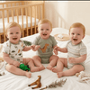 Three babies sitting on a bed with toys around them, smiling.