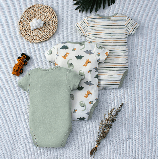 Three baby bodysuits with different patterns on a textured surface.