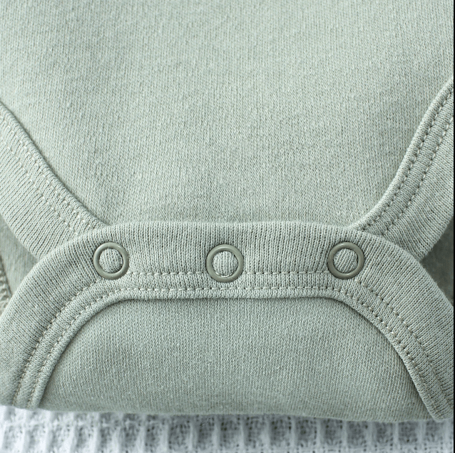 Close-up of a light green baby romper with button details on a textured fabric background.