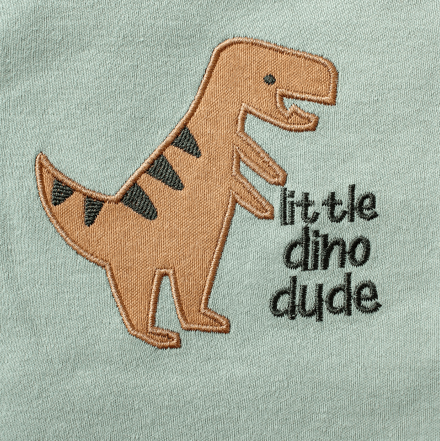 Embroidered dinosaur design with 'little dino dude' text on a light green background