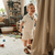 Child in a white outfit standing in a living room with toys on the floor.