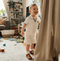 Child in a white outfit standing in a living room with toys on the floor.