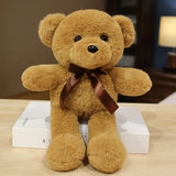 Brown teddy bear with a brown bow sitting on a wooden surface.