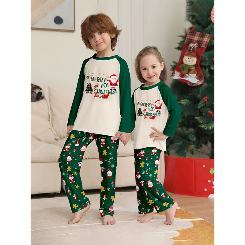 Two children wearing matching Christmas pajamas in a living room with a decorated tree.
