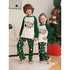 Two children wearing matching Christmas pajamas in a living room with a decorated tree.