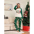 Woman wearing festive Christmas pajamas in a living room with a decorated tree.