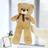 Brown teddy bear with a heart tag in front of white blinds