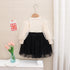 White long-sleeve top and black tulle skirt set on a hanger against a neutral background.