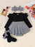 Black and white baby outfit with ruffled long-sleeve top, houndstooth skirt, socks, and headband on a textured surface.